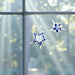 Two decorative handcrafted glass snowflakes hanging in front of a window with a blurred greenery background.