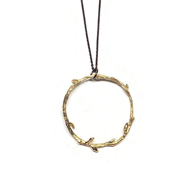 A gold necklace with a round pendant featuring a design of vines and branches, attached to a black sterling chain with a 3-inch extension.