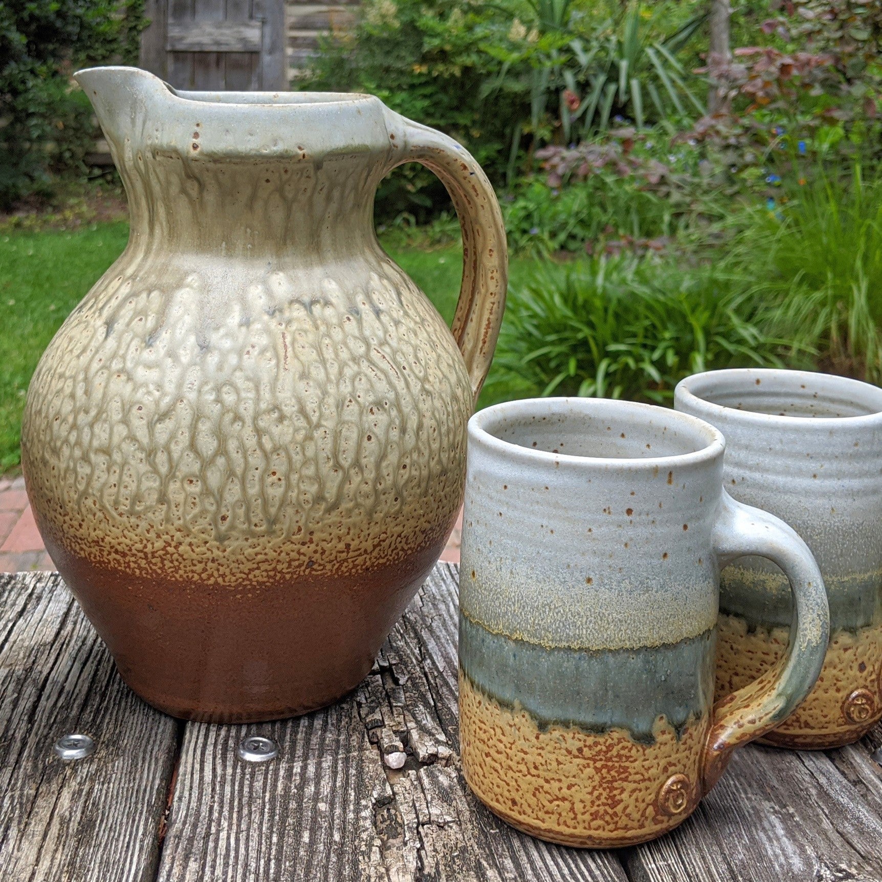 A ceramic pitcher and two mugs with a brown and greenish crackled glaze, displayed on a wooden surface.